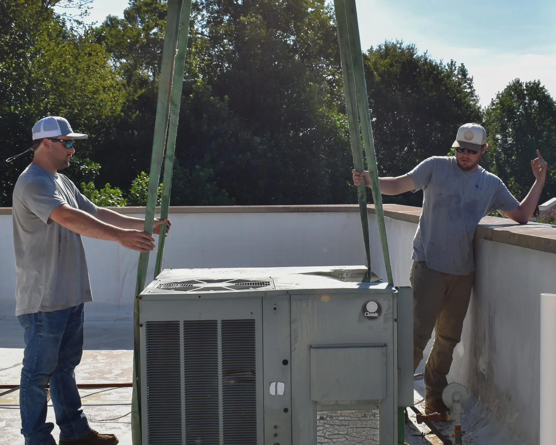 Upstate Climate Solutions employees informing the crane operator of where to put the HVAC system on the roof - HVAC system is on a pulley system