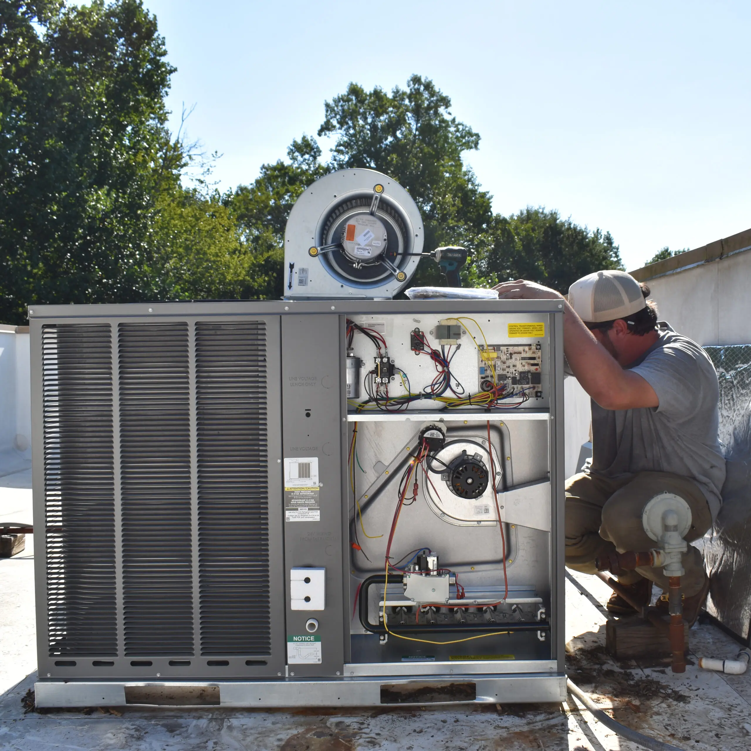 Upstate Climate Solutions' owner, Draysen Turner working on a residential HVAC system on the roof of an apartment building - kneeling on the ground inspecting behind the system